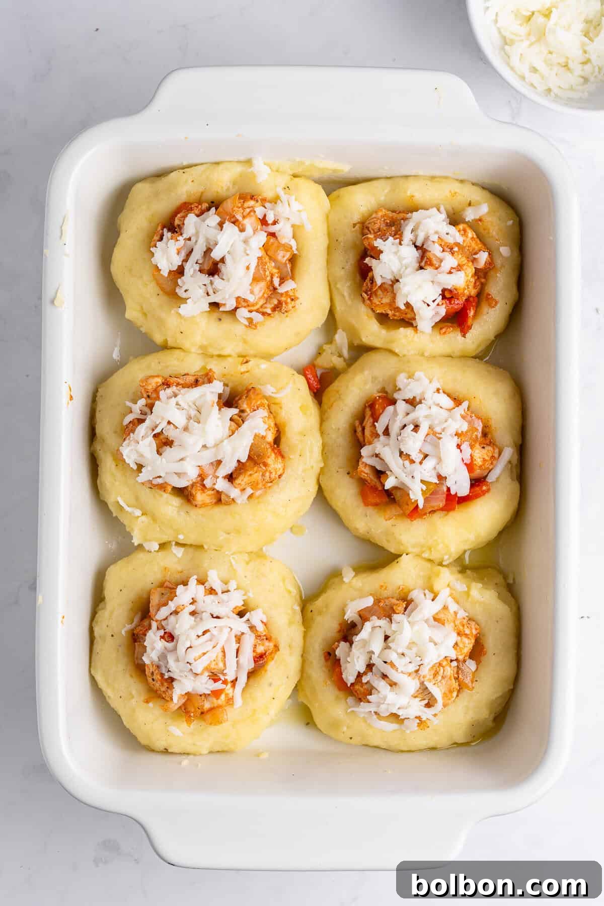 A baking dish with six mashed potato nests filled with a chicken cubes and vegetable mixture and topped with grated cheese. 