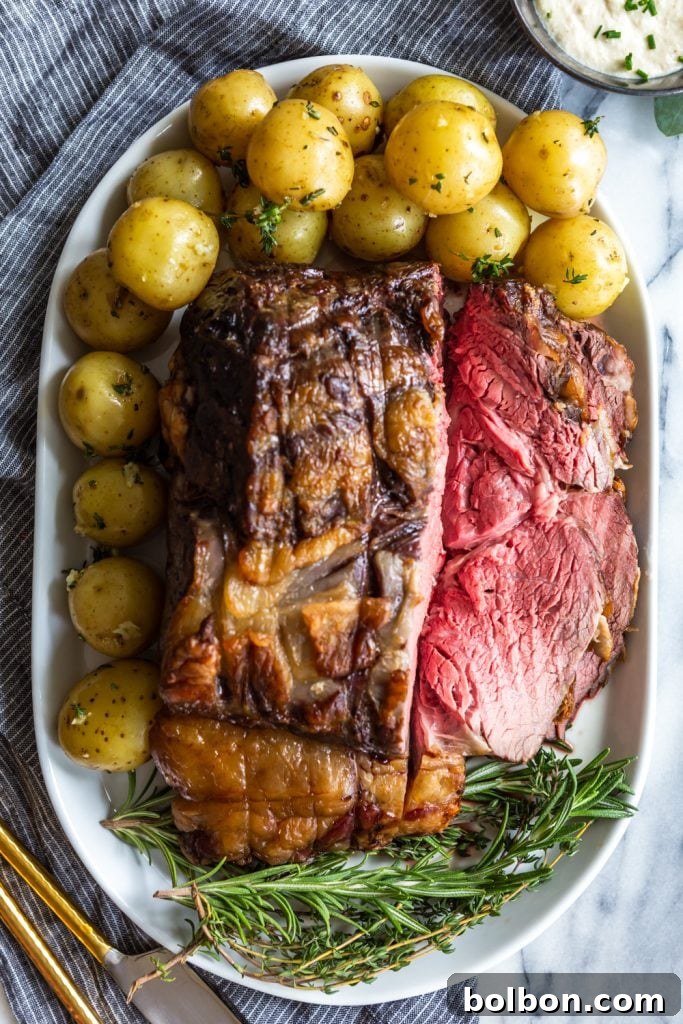 Slow Roasted prime Rib sliced showing pink interior, on a plate with baby potatoes and fresh herbs.