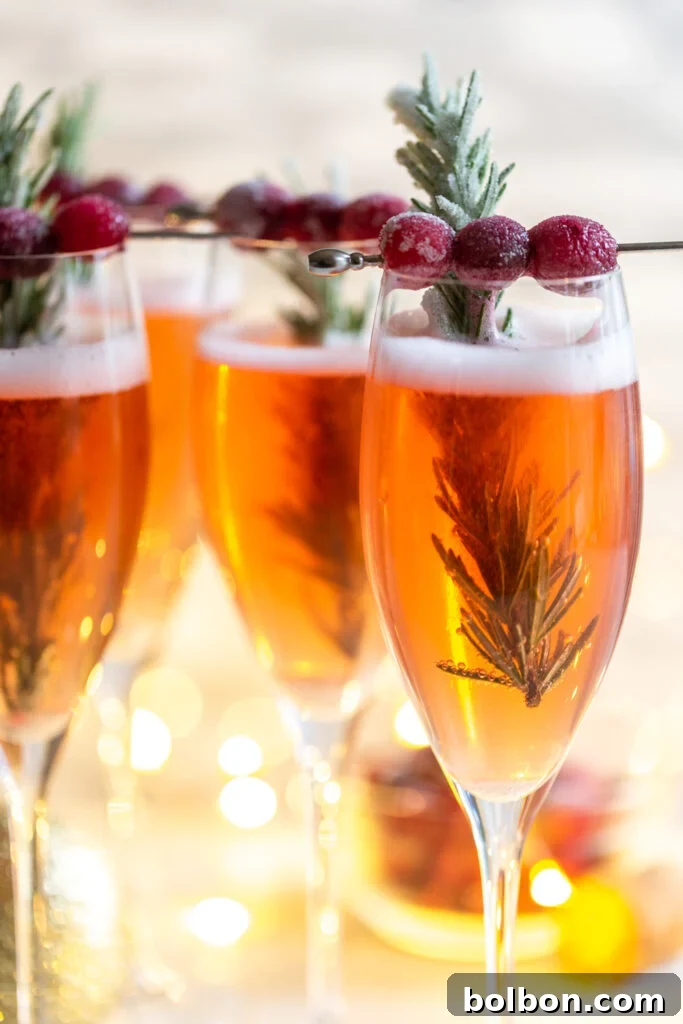 Cranberry Mimosa in a champagne flute, garnished with sugared cranberries and rosemary. 