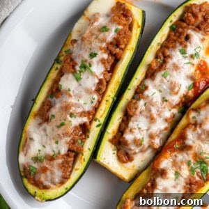 Three Stuffed Zucchini Boats filled with a hearty meat sauce, topped with melted cheese and chopped herbs, and elegantly served on a white plate, perfect for a family dinner.