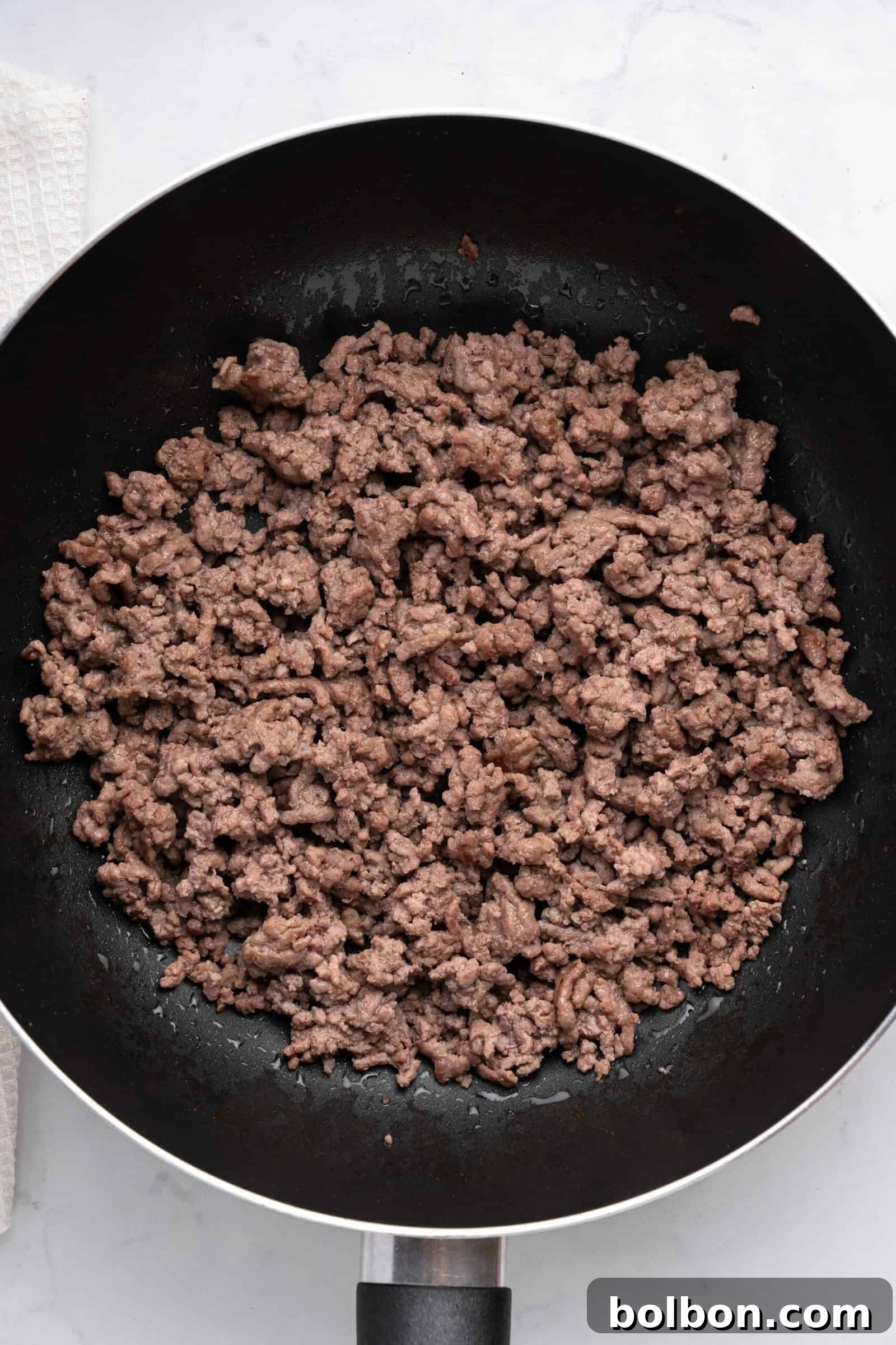 Loaded Zucchini Boats 6 A black frying pan filled with cooked, crumbled ground beef sits on a white countertop. The beef is browned and evenly distributed across the pan, creating a rich base for the zucchini boat filling.