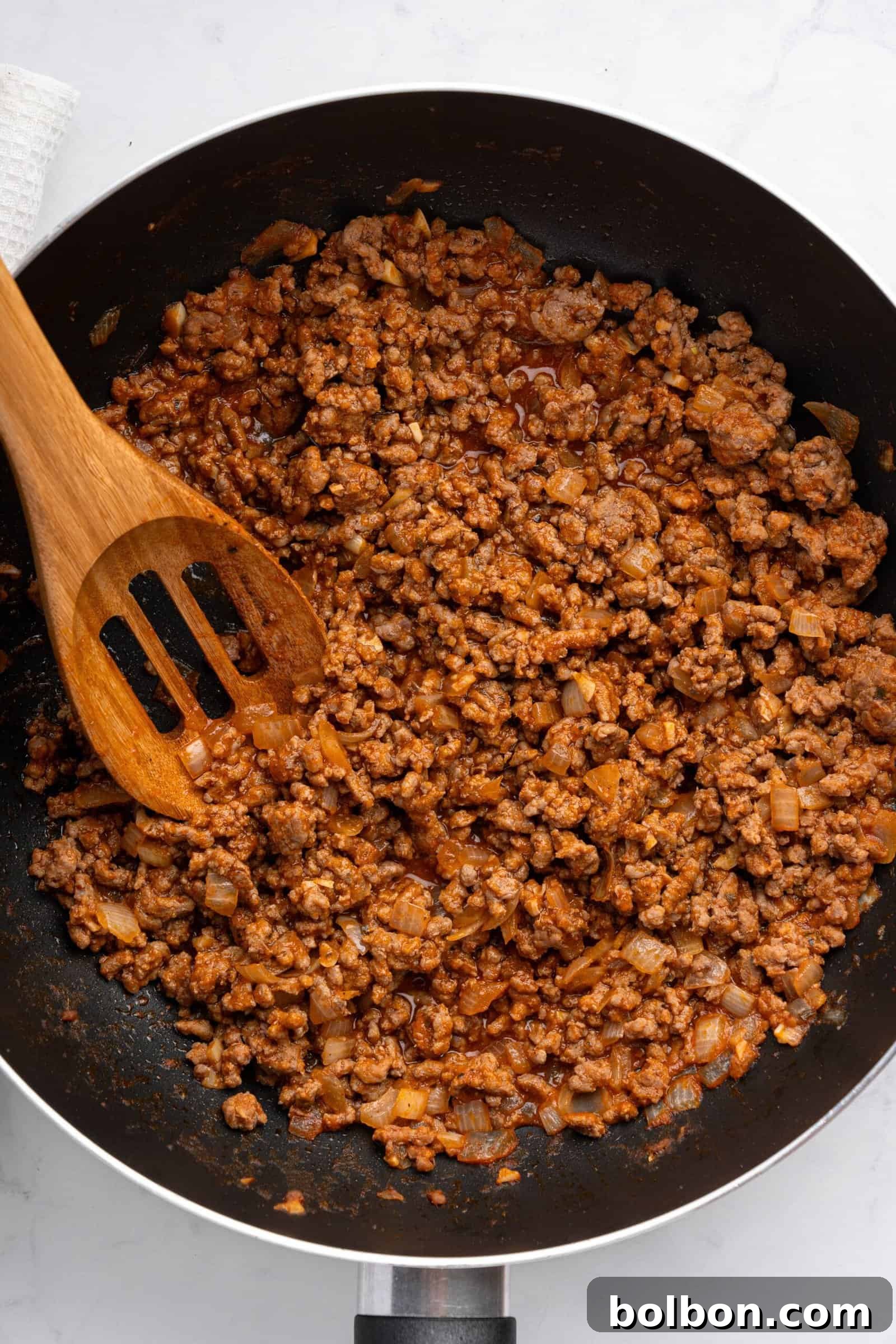 Loaded Zucchini Boats 8 A skillet filled with cooked ground beef mixed with diced onions and spices, with a wooden spatula resting on the side. The mixture appears well-seasoned and is slightly saucy, perfect for stuffing zucchini.