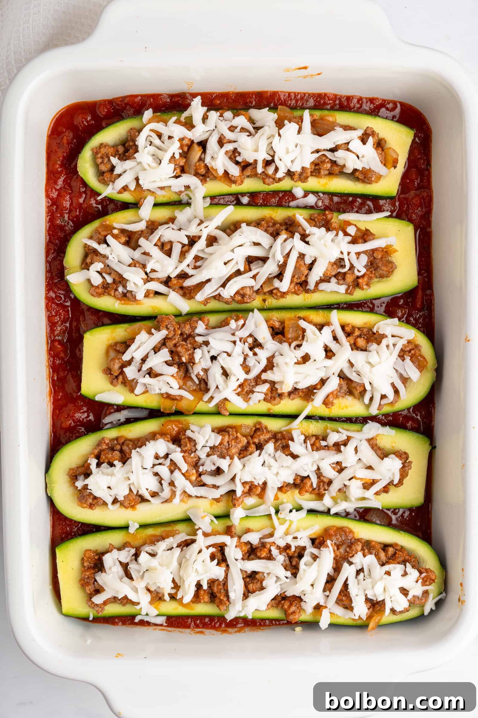 Loaded Zucchini Boats 10 A baking dish filled with zucchini halves stuffed with a mixture of ground meat and topped with shredded cheese. The dish is set in a base of tomato sauce, ready for baking to golden perfection.
