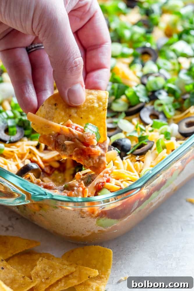 Seven Layer Fiesta Dip 5 Tortilla chip dipping into 7 layer dip
