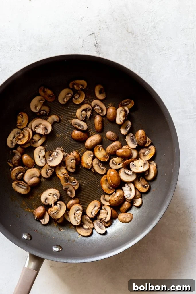 Mushrooms in a hot, dry pan, releasing their moisture during the essential dry-sautéing process.