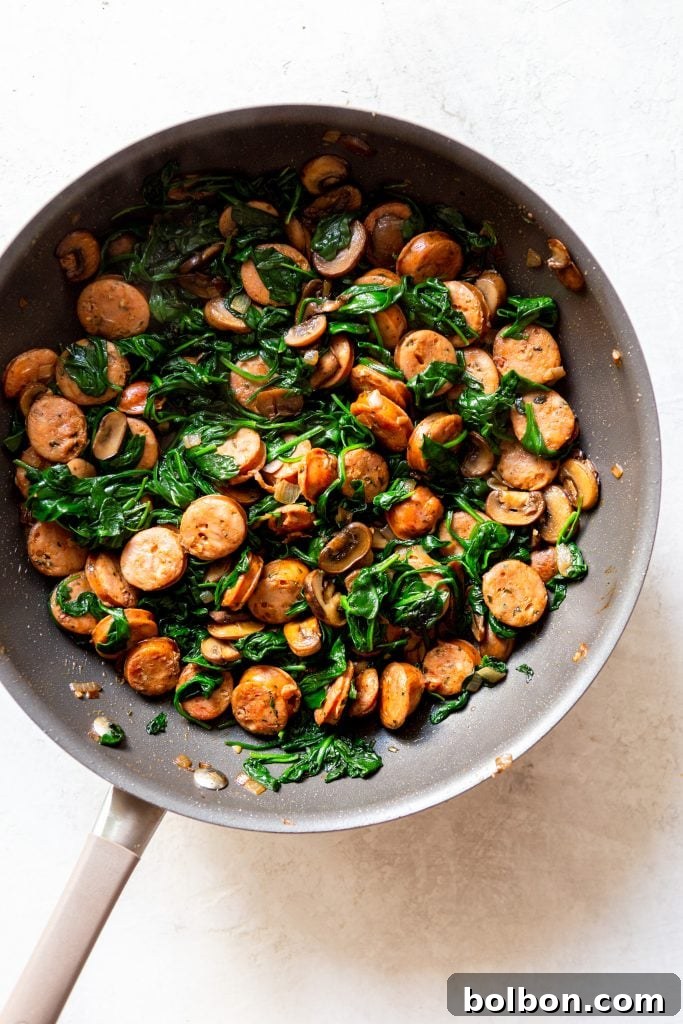 Fresh baby spinach being added to the hot pan, ready to wilt into the pasta mixture.