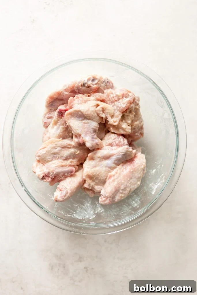 Crunchy Oven-Baked Chicken Wings 4 Raw chicken wings in a glass bowl, tossed with baking powder and salt.