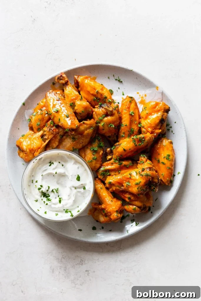 Crunchy Oven-Baked Chicken Wings 9 Baked buffalo wings with two sauces - original buffalo sauce and honey buffalo sauce. On a white plate, next to a small bowl of creamy yogurt dip.