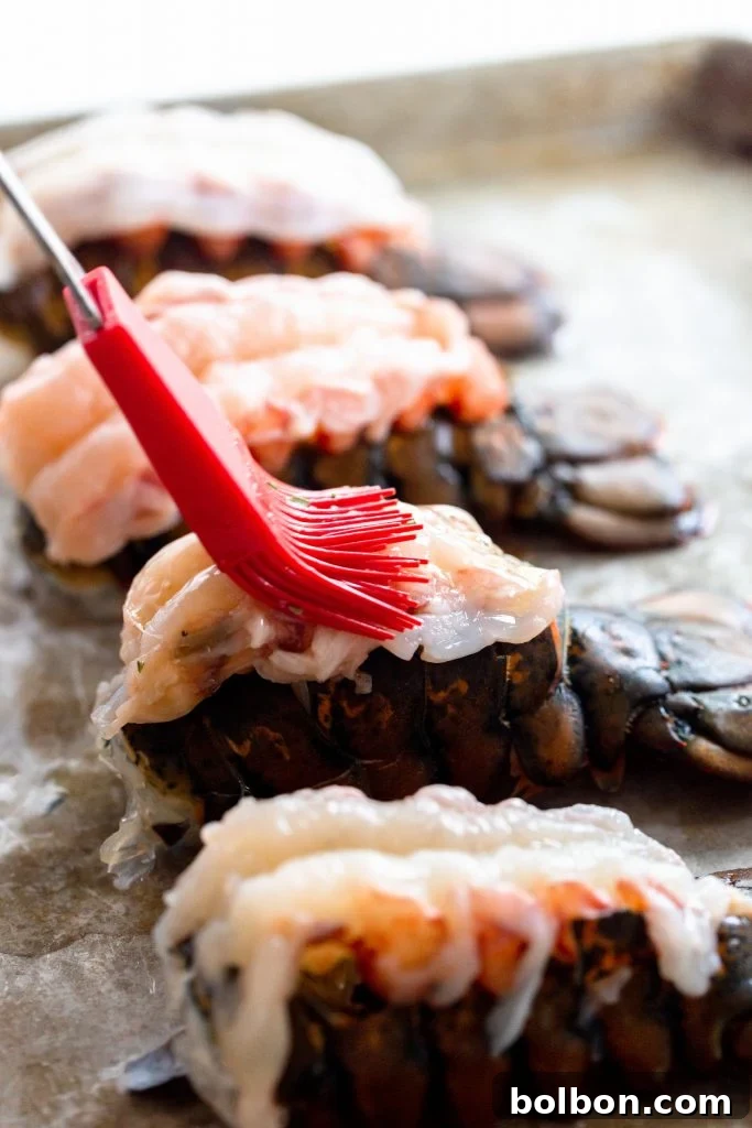 Chef brushing melted garlic herb butter onto a raw butterflied lobster tail