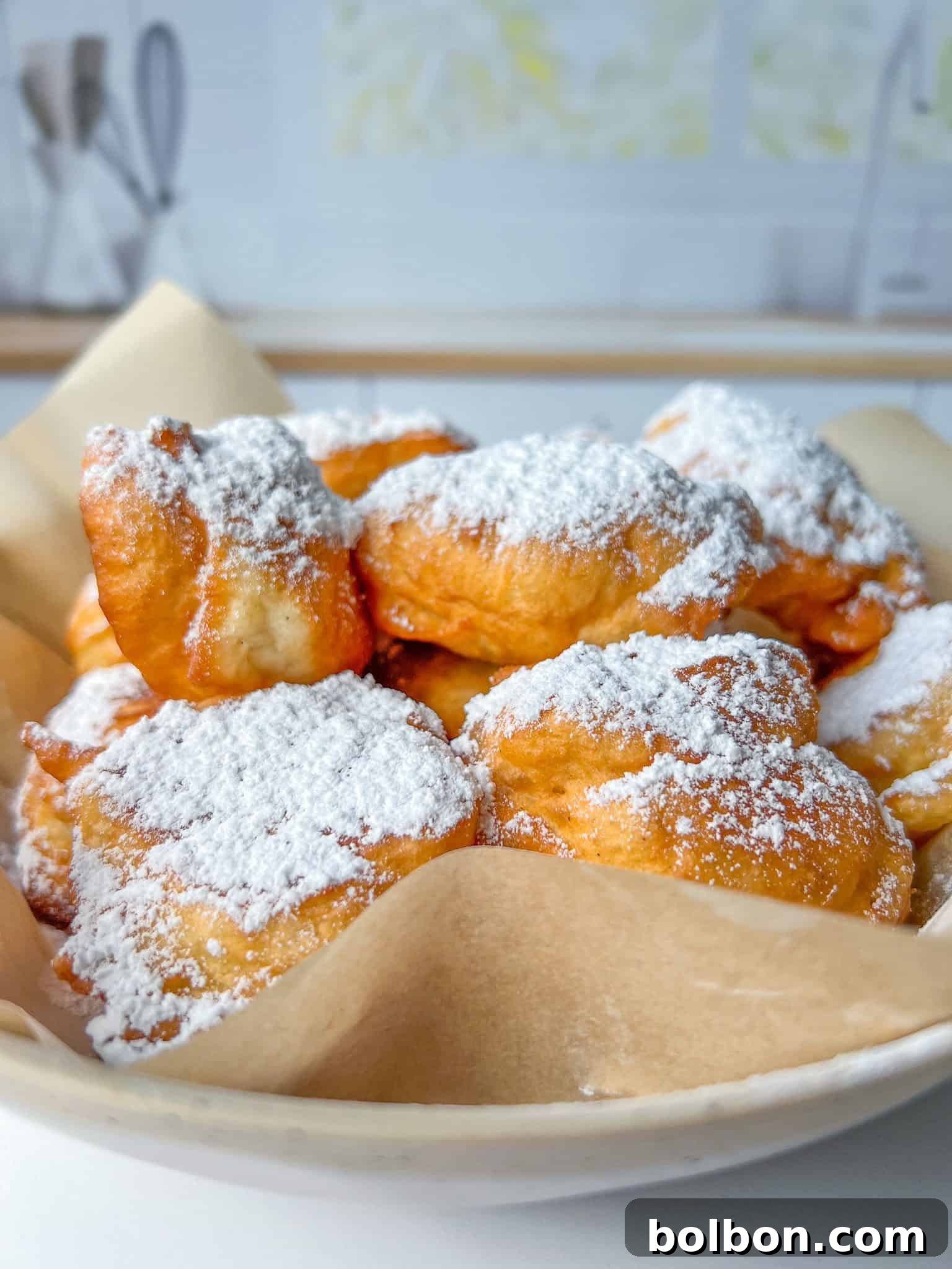 Golden Bulgarian Fritters 3 A pile of golden, powdered sugar-dusted Mekitsi on a wooden board with a cup of coffee