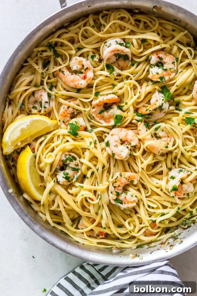 Shrimp Scampi Pasta in a stainless steel pan, garnished with lemon wedges, ready to be served.