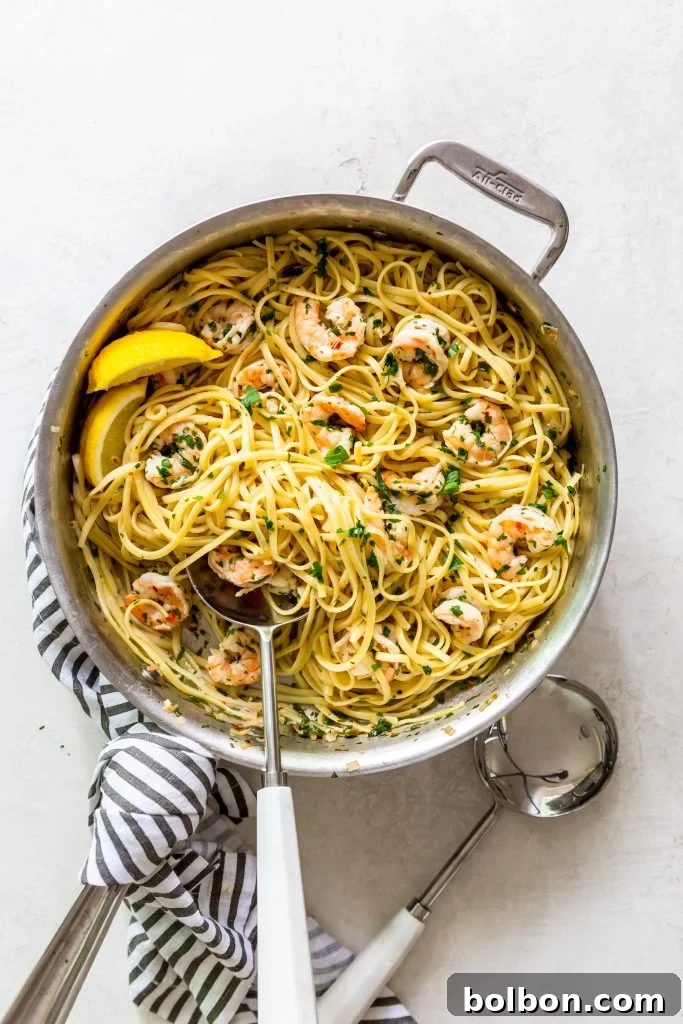 Close-up of Shrimp Scampi Pasta glistening in a stainless steel sauté pan, showcasing the rich garlic butter sauce and perfectly cooked shrimp.