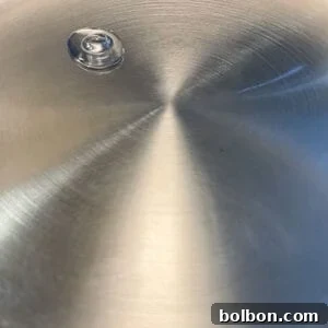 A single drop of oil sits on the shiny surface of a stainless steel frying pan, reflecting light, illustrating how to make stainless steel non stick.