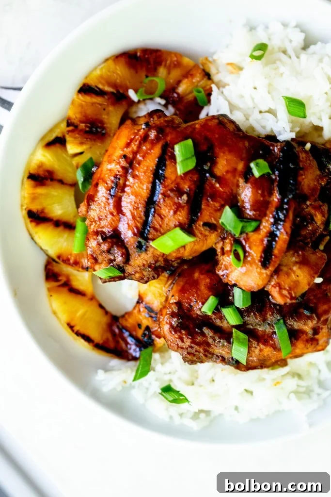 Grilled huli huli chicken on a bed of white rice with slices of grilled pineapple