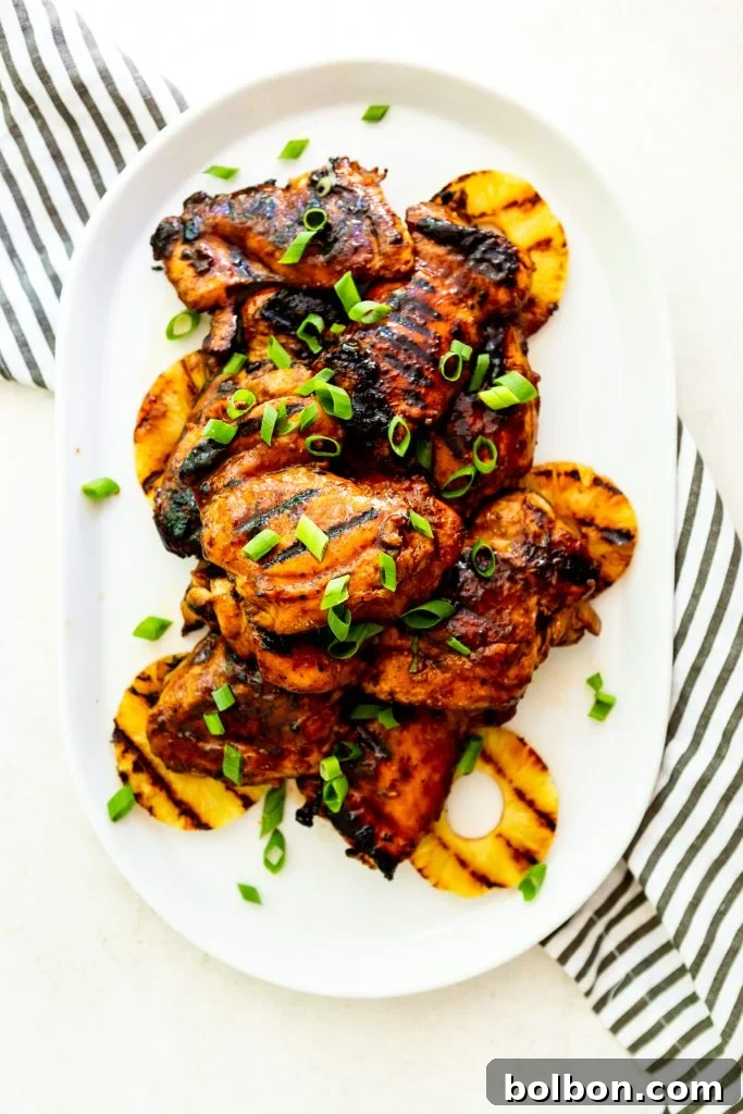 Grilled huli huli chicken thighs and grilled pineapple piled on a white platter, garnished with green onions.