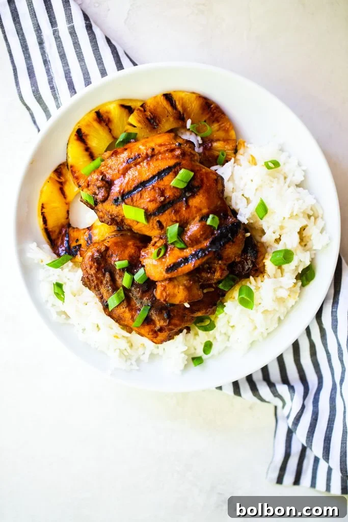 A plate of huli huli chicken on top of rice and grilled pineapple, garnished with green onions.