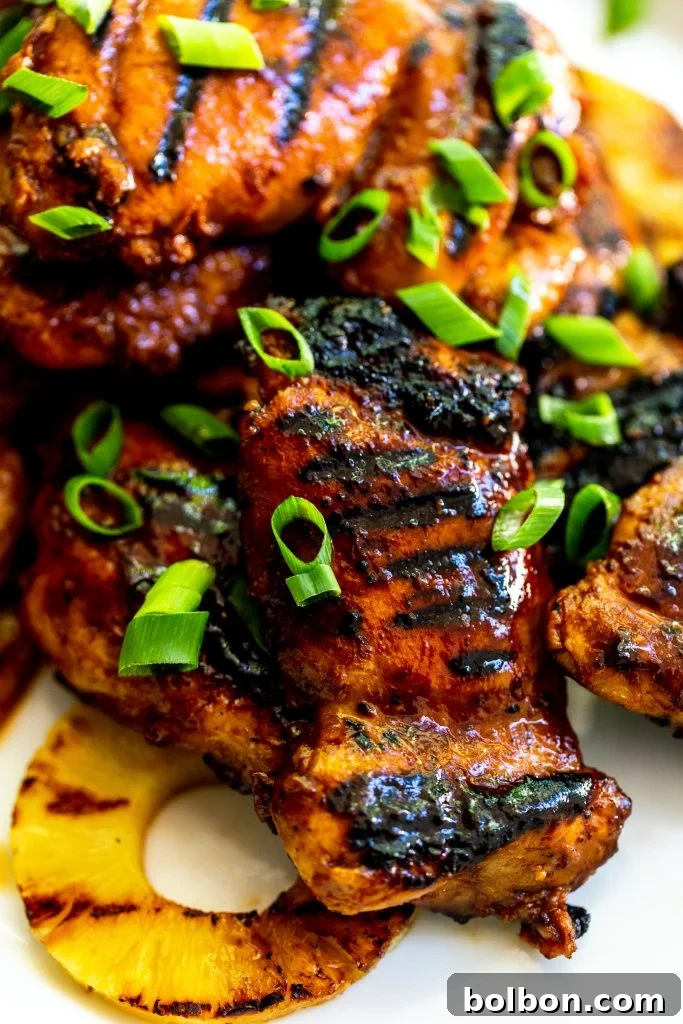 Close up of a char grilled huli huli chicken thigh, brushed with sauce, garnished with green onions. 