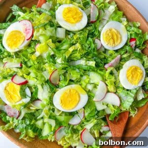 A Simple Green Salad is served in a wooden bowl, featuring chopped lettuce, sliced radishes, and hard-boiled egg slices, accompanied by two wooden salad servers.