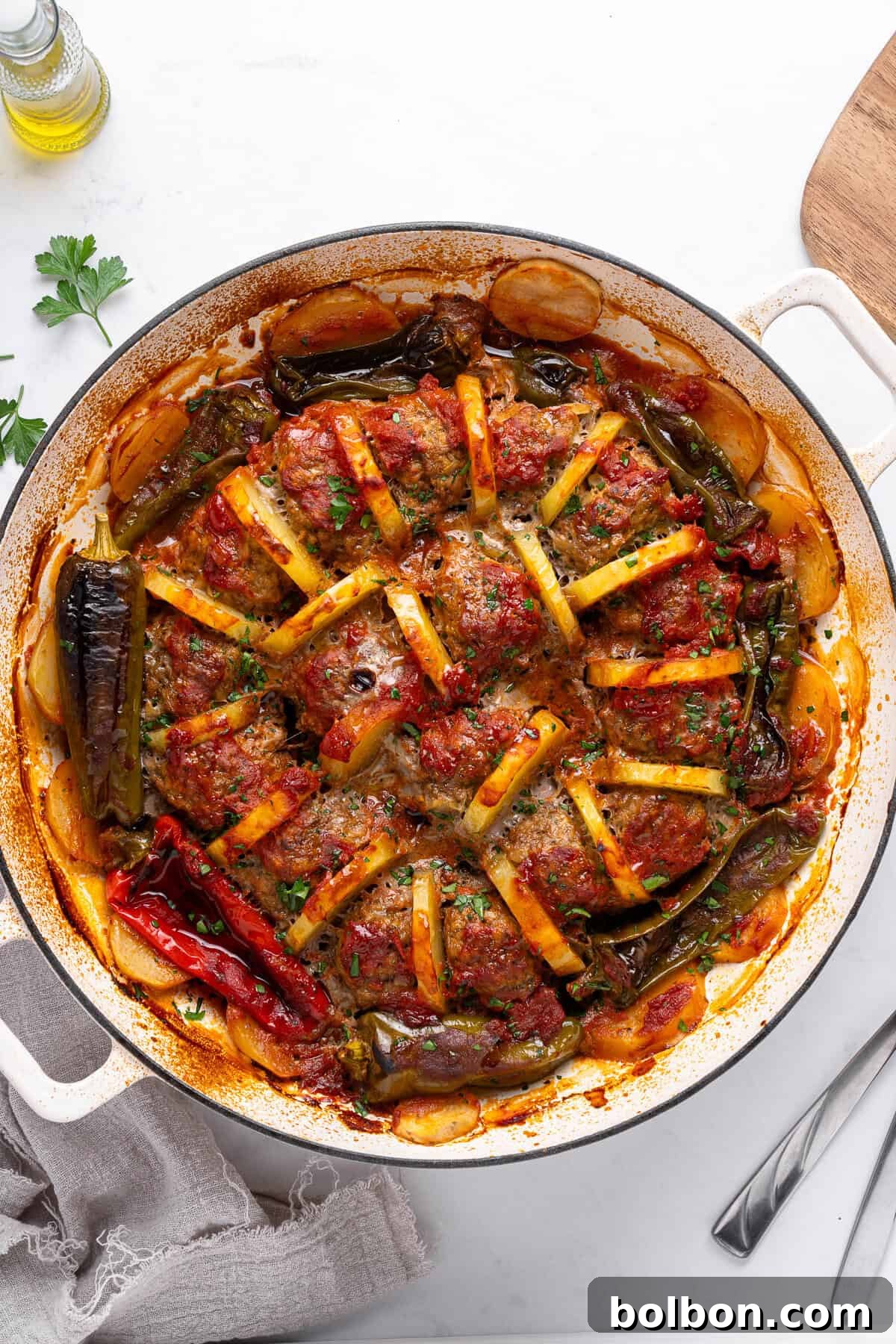 A round baking dish filled with baked vegetables, arranged in a star pattern. Includes tomatoes, potatoes, and peppers, topped with herbs. The dish is on a white surface with a napkin and a fork nearby.