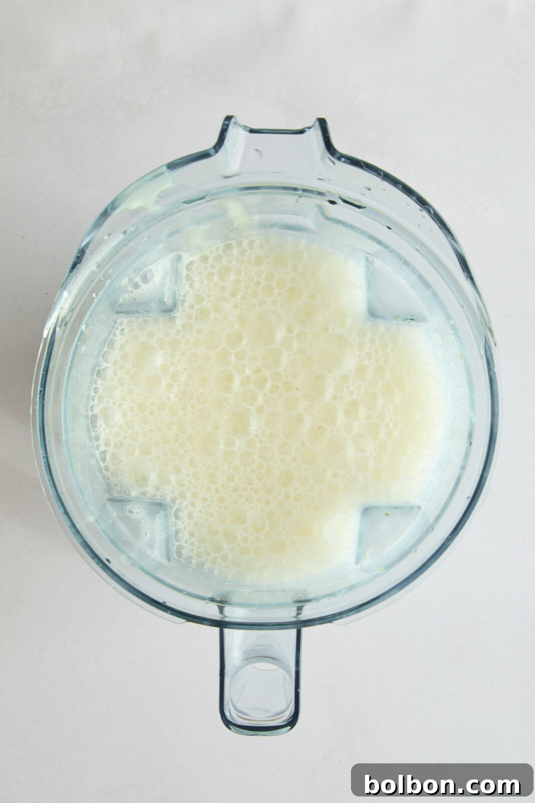 A top-down view of a blender filled with foamy Brazilian Lemonade, likely a smoothie or milkshake. The clear blender jug contrasts with the white background, highlighting the bubbles on the surface of the liquid.
