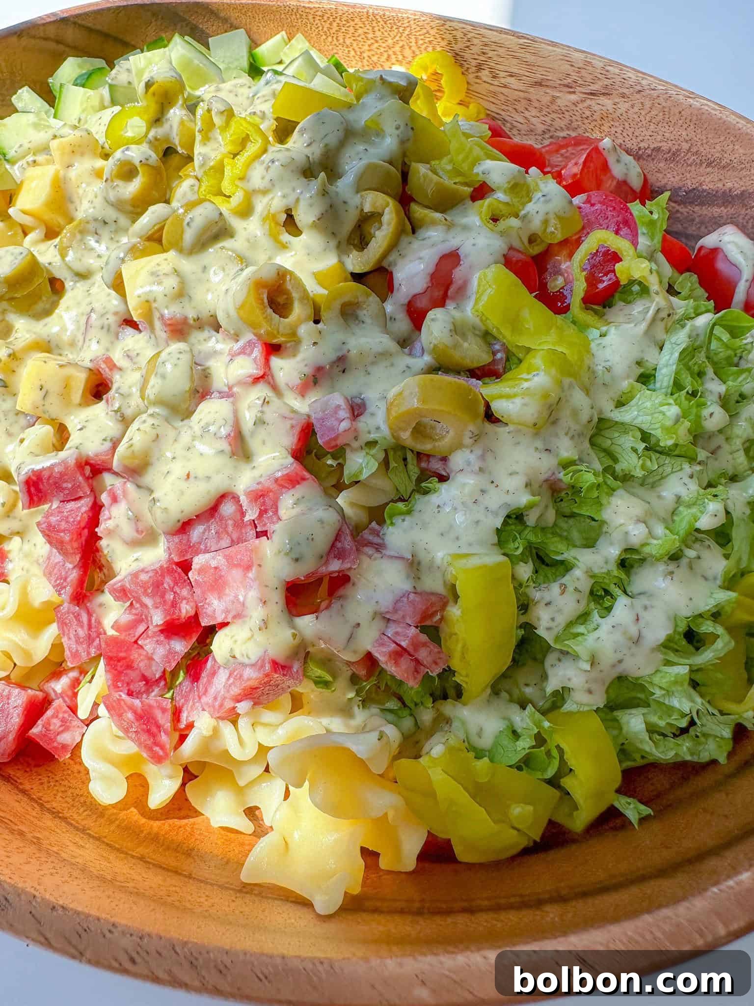 Deli Grinder Pasta Salad 2 A vibrant bowl of Italian Grinder Pasta Salad, featuring pasta, shredded lettuce, salami, cheese cubes, cherry tomatoes, cucumbers, green olives, and pepperoncini, all coated in a rich, creamy dressing, ready to be served at a summer picnic.