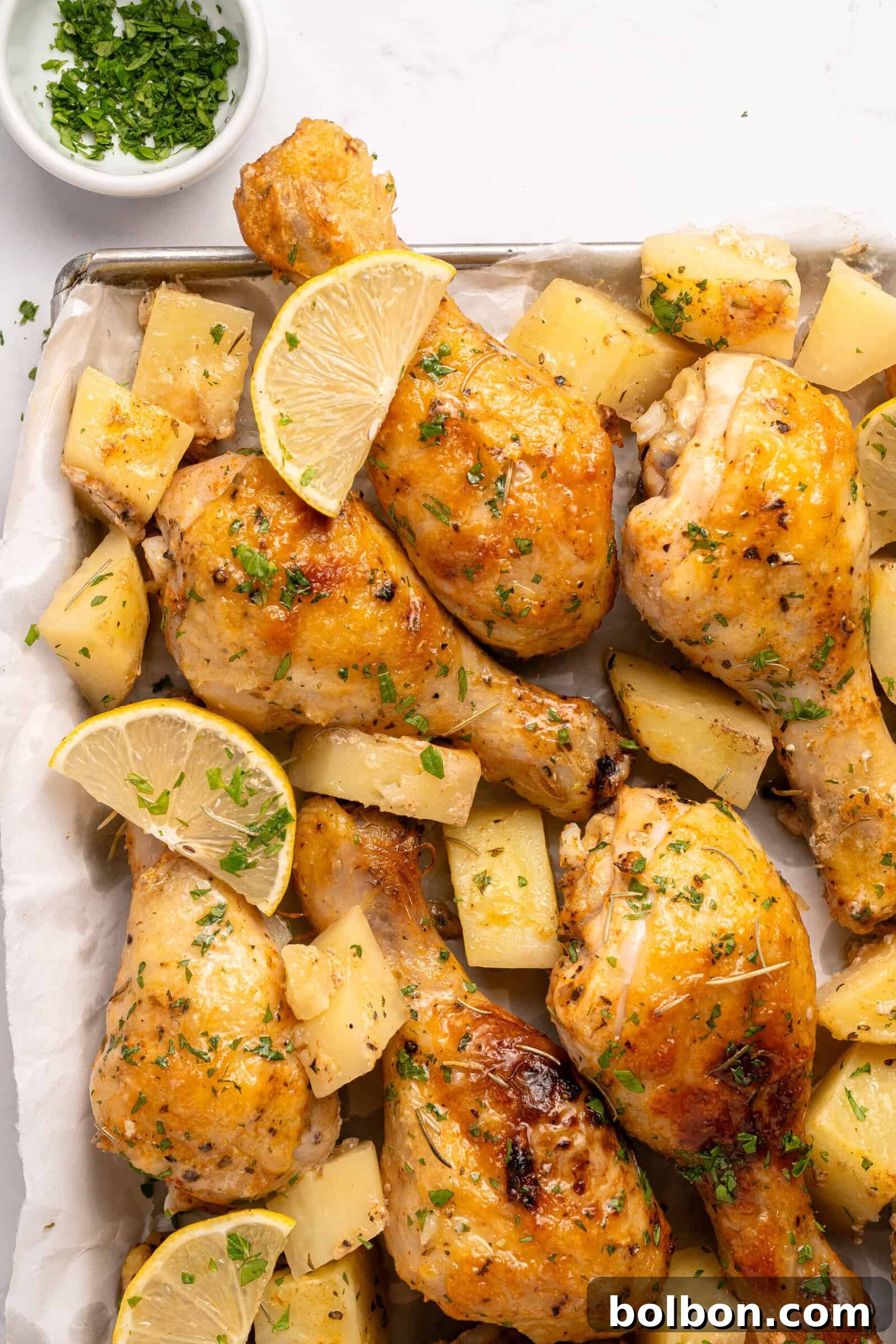 Golden Parmesan Chicken 2 A tray full of baked parmesan chicken and golden roasted potatoes, garnished with fresh herbs.