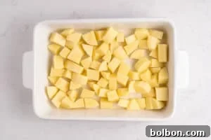A white rectangular baking dish filled with evenly cut raw potato cubes, placed on a light-colored countertop.
