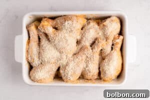 A white baking dish filled with raw, breaded chicken drumsticks, prepared for Baked Parmesan Chicken, arranged closely together and ready to be baked on a light marble surface.