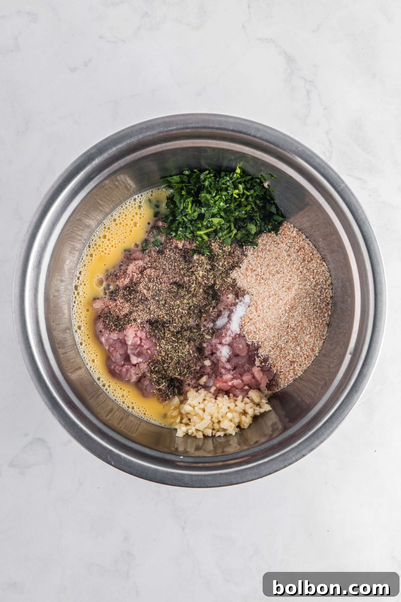 Next-Level Turkey Burgers 4 A metal bowl containing the initial mixture of raw ground meat, breadcrumbs, chopped dill, garlic, and spices, before the addition of feta cheese, on a marble surface.
