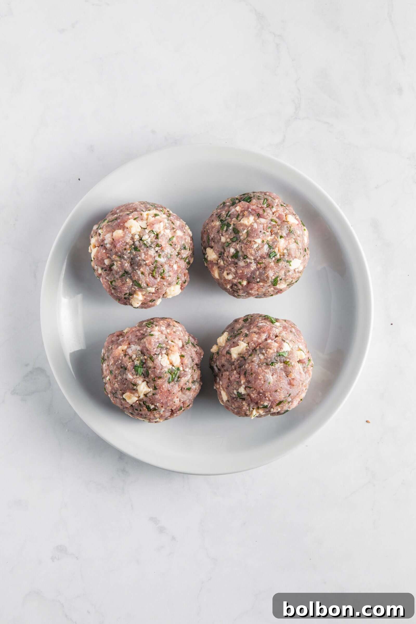 Next-Level Turkey Burgers 7 Four perfectly portioned raw turkey burger mixture balls on a white plate, seasoned and ready to be flattened.