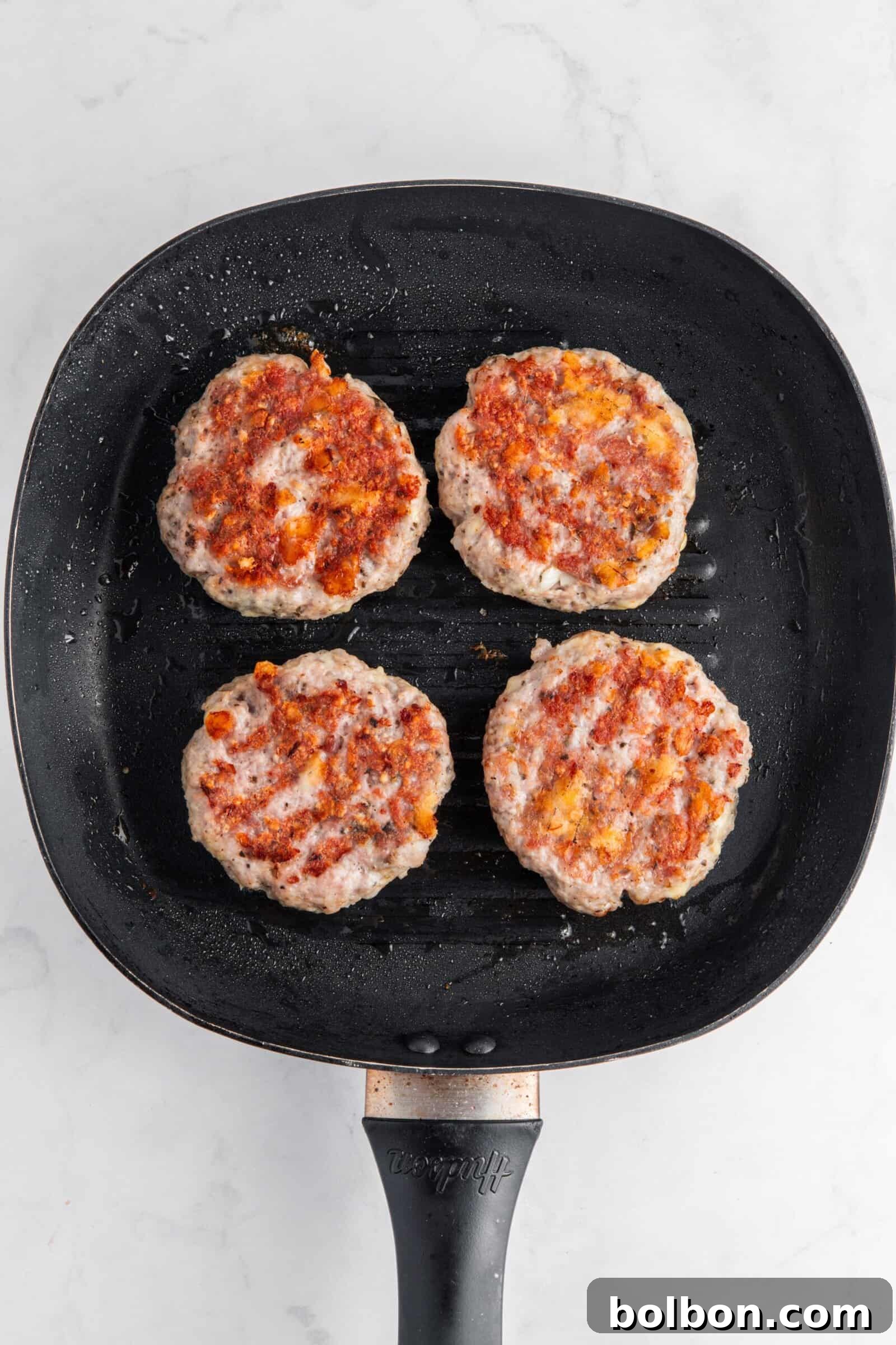 Next-Level Turkey Burgers 9 Four seasoned turkey burger patties sizzling on a hot, oiled barbecue grill, showing beautiful grill marks and browning.