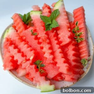 A plate of crinkle-cut Watermelon Fries garnished with fresh mint and thyme leaves, set on a light background, makes for a refreshing watermelon snack.