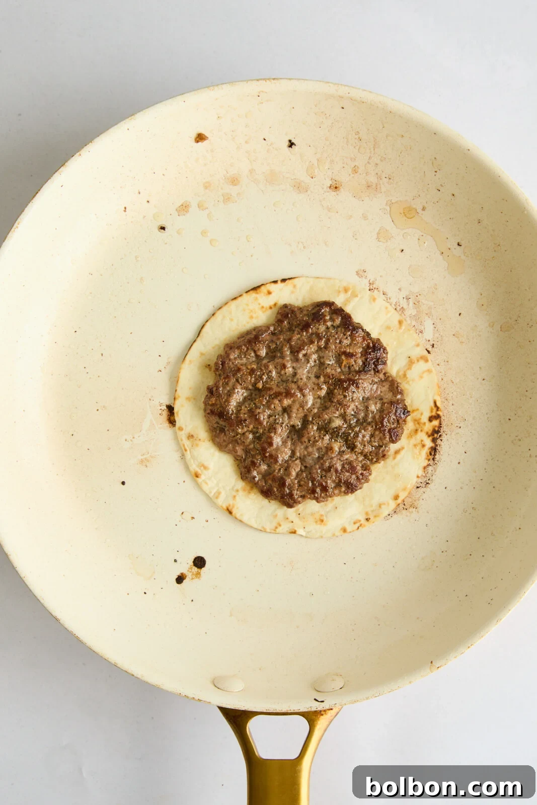 A Big Mac Smash Taco in the pan, cooked to golden perfection with a crispy meat crust, just before flipping.