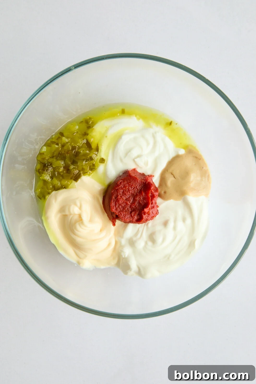 All the Mac Sauce ingredients, including mayonnaise, sour cream, yogurt, tomato paste, honey Dijon, relish, and pickle juice, are neatly arranged in a mixing bowl before being combined.