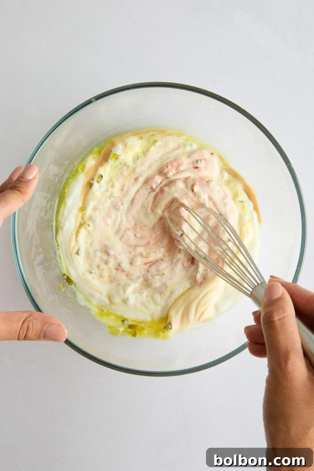A hand whisking together the creamy ingredients for the homemade Mac Sauce in a mixing bowl.
