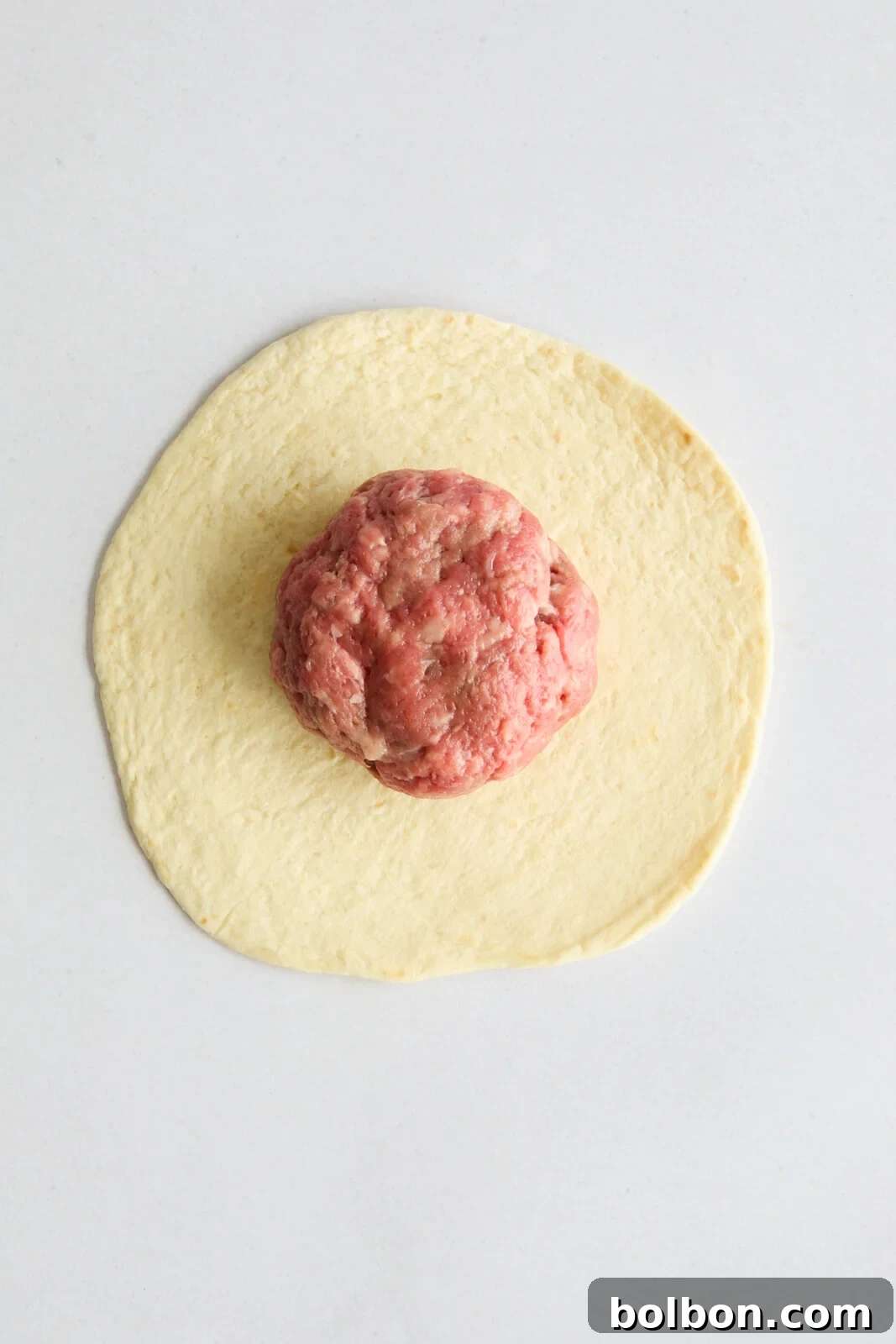 A small flour tortilla with a single, perfectly rolled ball of ground beef placed centrally on top, before being smashed.