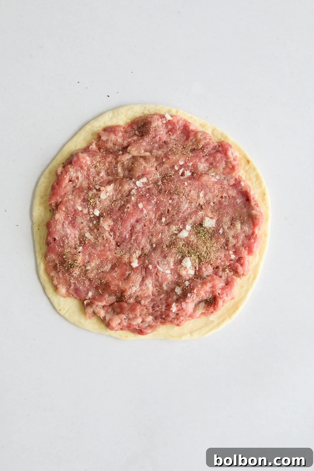 The ground beef is expertly pressed onto a flour tortilla, forming a perfectly even and thin layer, ready to be cooked as a smash taco.