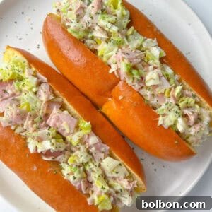 Two soft sandwich rolls filled with a creamy Italian Chopped Sandwich mixture of ham, lettuce, and herbs are served on a white plate.