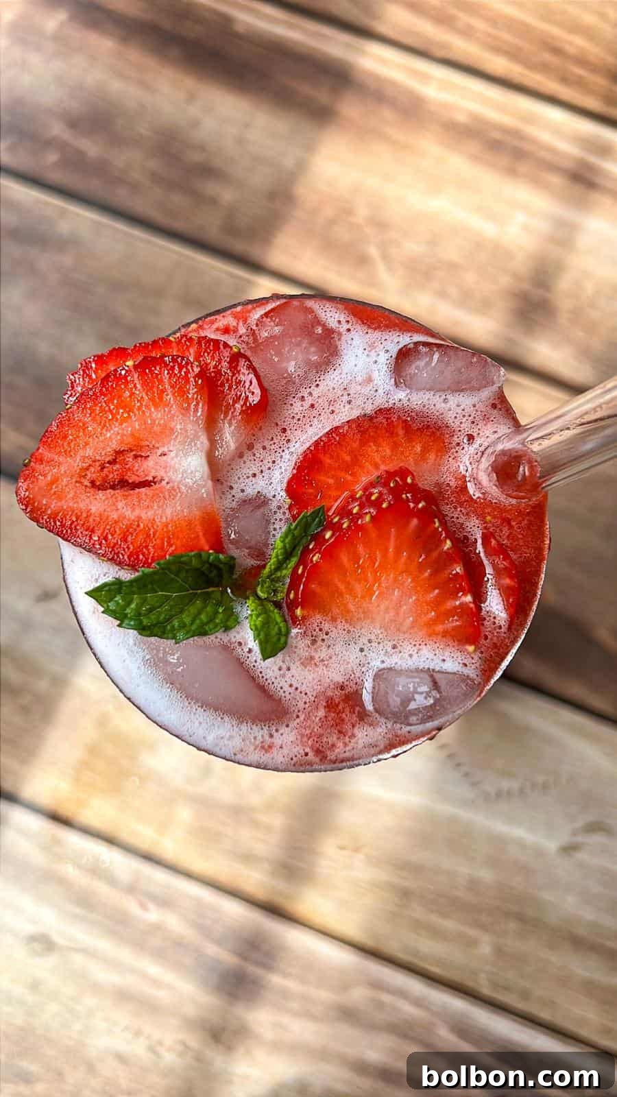 Fresh Strawberry Splash 2 A refreshing drink with ice, garnished with fresh strawberry slices and a sprig of mint, served in a glass on a wooden surface.