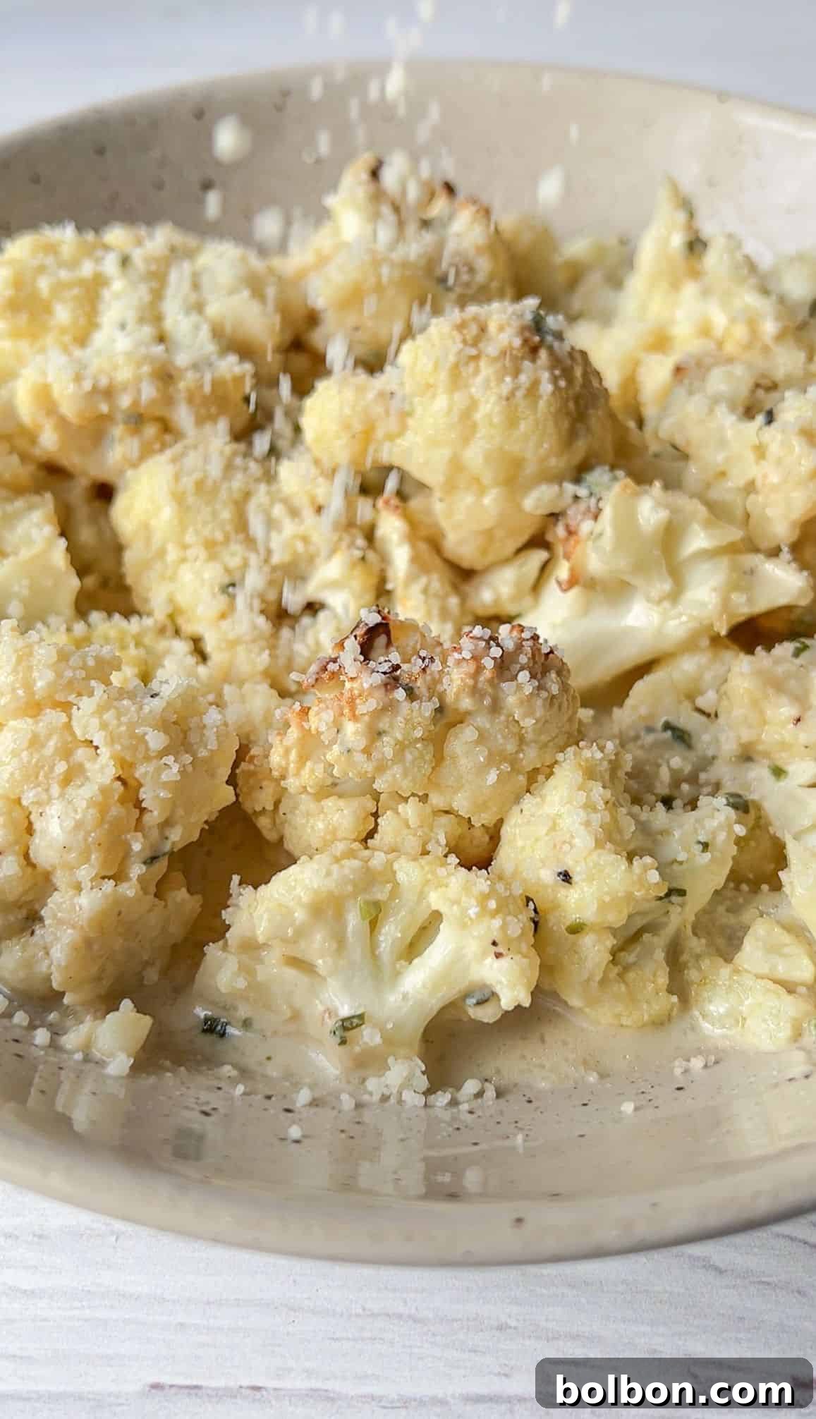 Golden Cauliflower Bake 7 A vibrant close-up of the finished Cheesy Baked Cauliflower Dish, generously sprinkled with grated Parmigiano Reggiano cheese. The cauliflower exhibits a beautiful golden-brown char on the edges, and the creamy, herb-flecked coating is clearly visible, promising rich flavor.