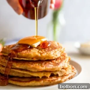 A perfectly golden stack of carrot cake pancakes with syrup pouring over them.
