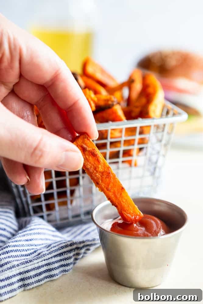 A perfectly crispy sweet potato fry being dipped into a dollop of vibrant red ketchup.