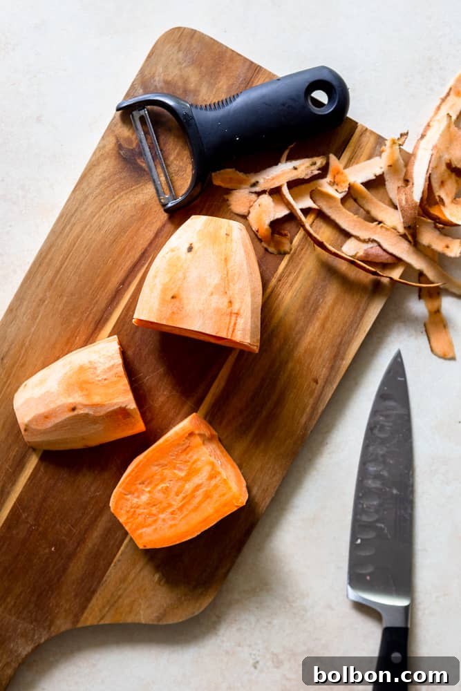 A sweet potato being peeled with a vegetable peeler.