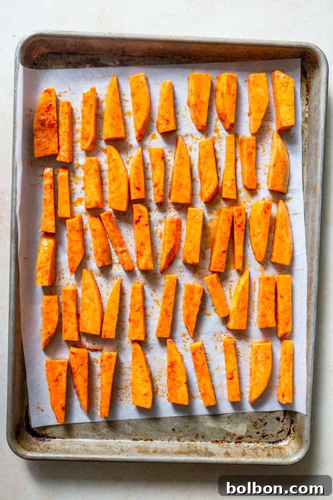 Sweet potato fries spread in a single layer on a parchment-lined baking sheet, ready for the oven.