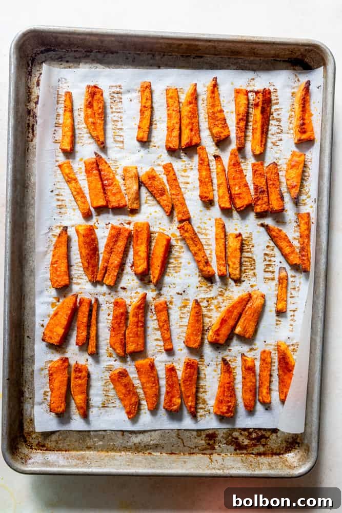 A baking sheet filled with sweet potato fries halfway through baking, showing early browning.