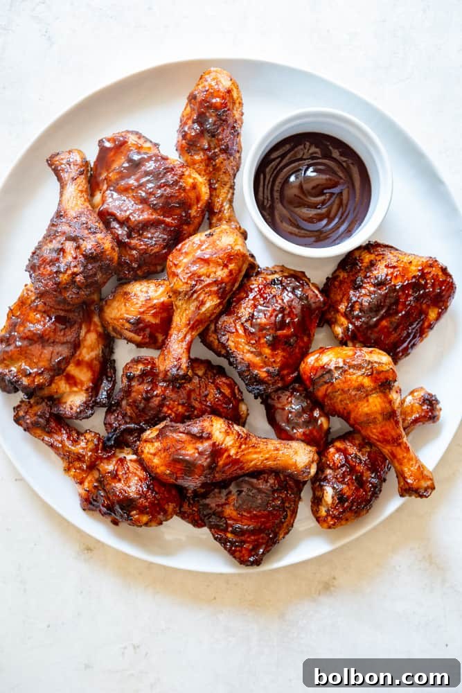 A large white platter generously filled with perfectly grilled BBQ chicken thighs and drumsticks, glistening with sauce and hints of a smoky char. It’s a feast for the eyes, showcasing the golden-brown skin and juicy texture that defines truly great barbecue.