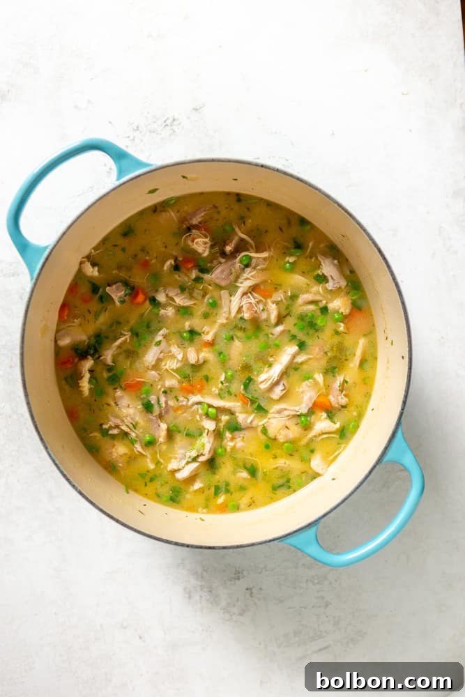 A rich, creamy chicken and dumpling soup, simmering gently in a Dutch oven, moments before the fluffy dumplings are added to complete the dish.