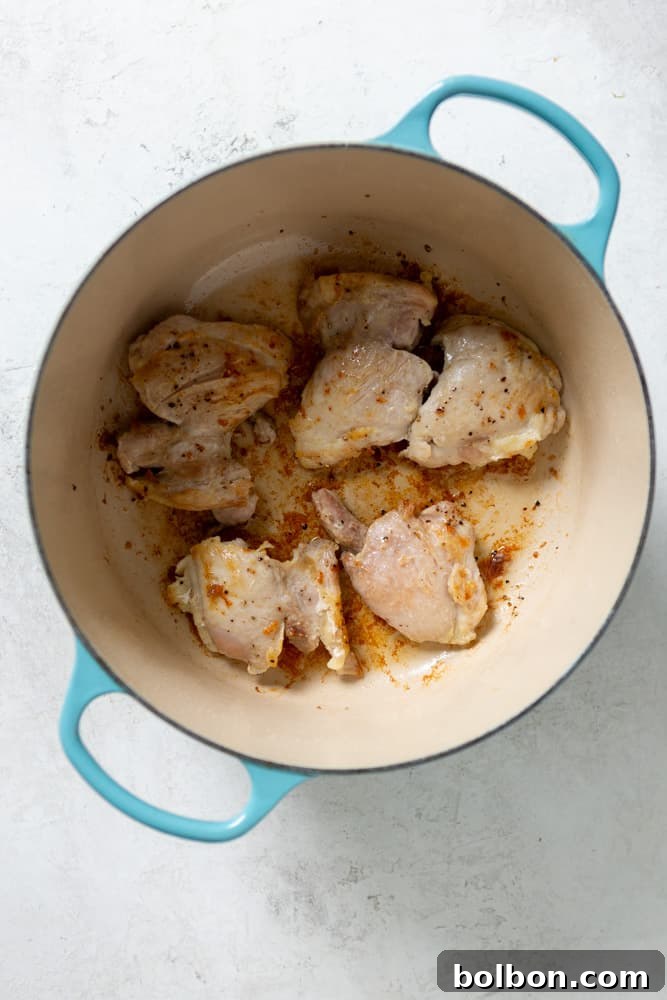 Chicken thighs being expertly browned to a golden crisp in a heavy Dutch oven, ready to release their rich flavor into the stew.