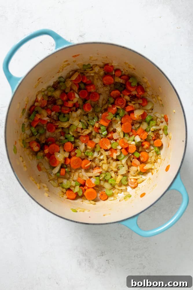 A vibrant mix of freshly chopped carrots, celery, and onions softening in a Dutch oven, forming the aromatic base of the chicken stew.