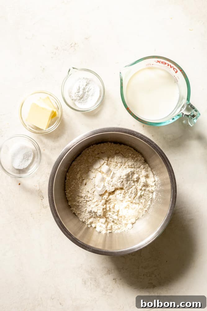 All the essential ingredients for making light and fluffy dumplings: neatly portioned flour, a measuring spoon of salt, a small bowl of baking powder, a stick of butter, and a glass of whole milk.